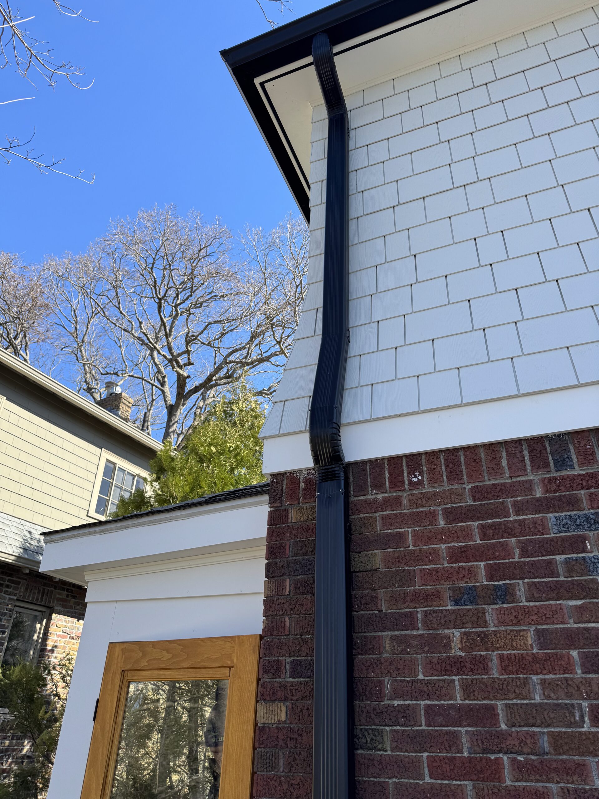 Black downspout on white shingle siding